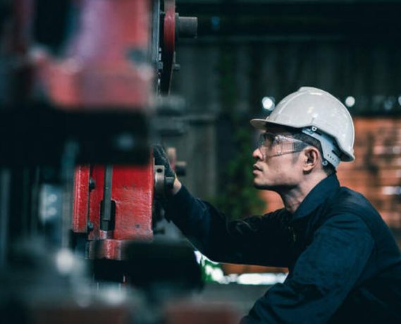 Men industrial engineer wearing a white helmet while standing in a heavy industrial factory behind. The Maintenance looking of working at industrial machinery and check security system setup in fact